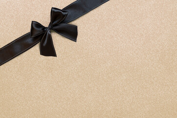 Black ribbon with bow isolated on gold glittering background. The concept for festive gift banner with place for text.