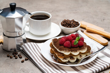 portion of Classic tiramisu dessert with raspberries, cup of espresso, coffee maker on grey concrete background