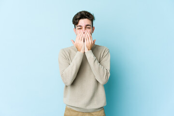 Young caucasian man isolated on blue background laughing about something, covering mouth with hands.
