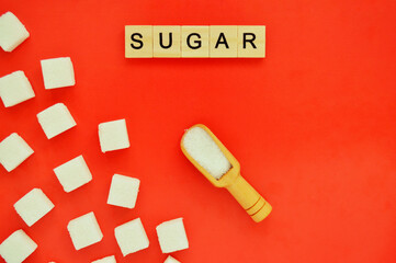 Refined sugar and wooden spoon with loose sugar on red background. Word sugar of wooden blocks with letters