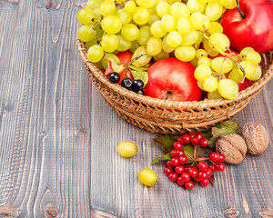 Ripe fresh colorful fruits and berries in a wicker  basket. Apples, grapes, berries, nuts on a wooden background with copy space. Thanksgiving day concept, autumn harvest.