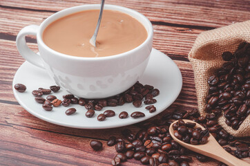 Hot  coffee stirrer in a white cup  on a table with coffee beans roasted in a bag and a wooden spoon.