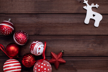 Christmas card. Red Christmas balls are scattered on a dark brown wooden background, and in the upper right corner is a white deer. Flat bed, top view, copy space. Christmas frame, new year's banner 