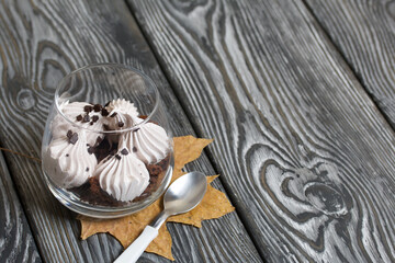 Zephyr in a glass. With biscuit and chocolate. Nearby are dried maple leaves. On pine boards painted black and white.