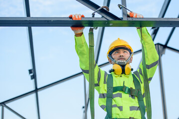 Asian construction worker Wear safety clothing and harnesses to do construction work on steel roof...