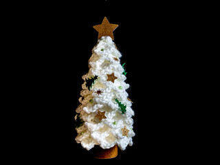 Árbol de navidad blanco, hecho a mano de ganchillo, con lana blanca, y con decoraciones pegadas y estrella dorada en la copa, sobre fondo negro.