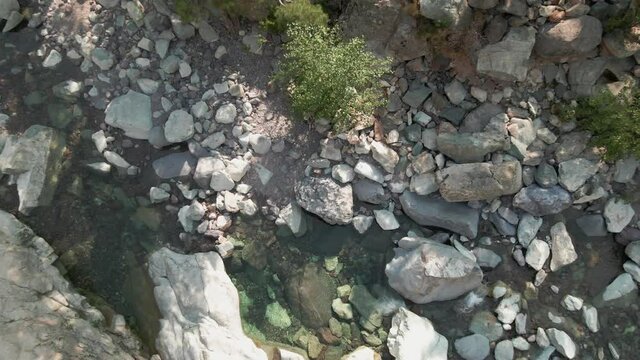Aerial view zooming out from crystal clear rocky mountain stream to view a road and ancient stone bridge at Asco on Corsica