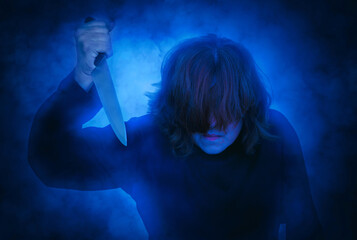 Frightening woman with hair covering her face holding a knife. Smoke effect applied. Halloween and horror concept.    