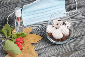 Zephyr in a glass. With biscuit and chocolate. Nearby are medical masks, an antiseptic and a hawthorn branch with red berries. On pine boards painted black and white.