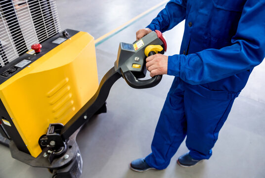 A worker in a warehouse uses a hand pallet stacker to transport pallets.