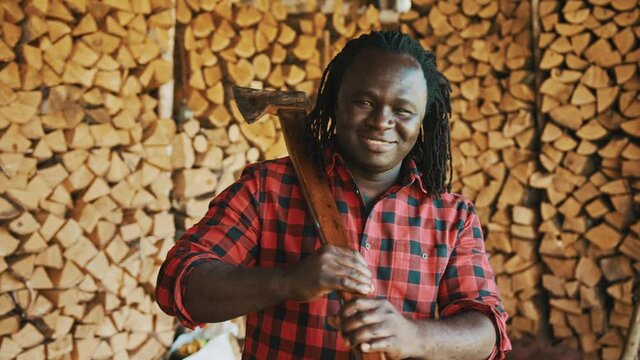 African man with the axe standing in front of stack of cutted timber for winter. High quality 4k footage