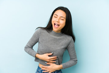 Young chinese woman isolated on a blue background laughs happily and has fun keeping hands on...