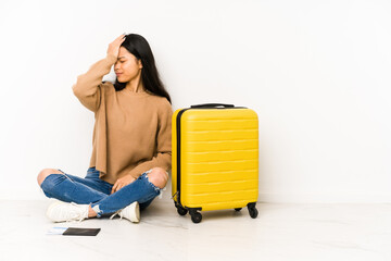 Young chinese traveler woman sittting on the floor with a suitcase isolated forgetting something, slapping forehead with palm and closing eyes.