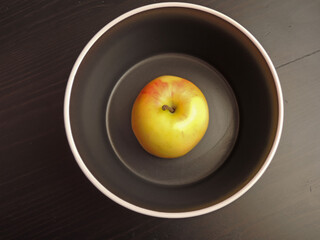 Apple in a black plate on a black wooden background.