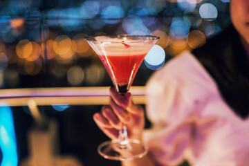 cocktail cosmopolitan in woman hand with bokeh