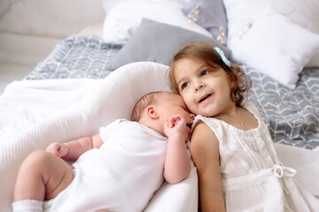 Beautiful little sister 2 years old looks at newborn brother lying on the bed in the bedroom at home