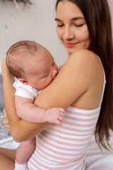 Young beautiful brunette mom holds a newborn baby in her arms