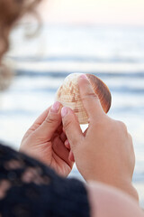 A woman gently holds a seashell in her hands at the sea.