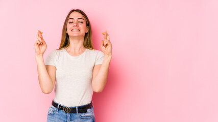 Young caucasian woman isolated on pink background crossing fingers for having luck