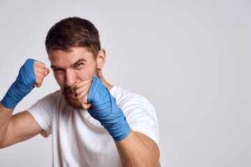 A sportive man in a white T-shirt boxing bandages on his hands practicing blow exercises improving skills