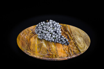 A bunch of white grapes on a large round wooden plate. Black matte background.