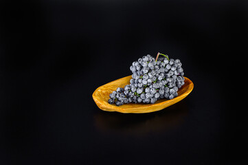 A bunch of white grapes on a small oval wooden plate. Black matte background.