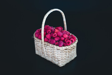 Fototapeta na wymiar Ripe raspberries in a white wicker basket on a black background.