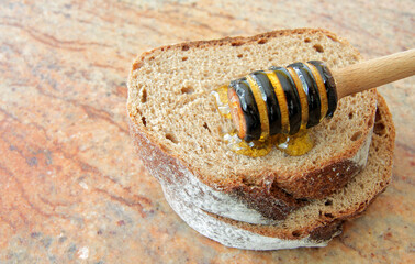 
a honey dipper with lime honey lies on a slice of bread on a granite table.