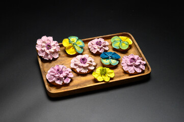 Cookies decorated with sugar flowers in different colors. Cookies on a wooden rectangular plate. Black background with a single light source.