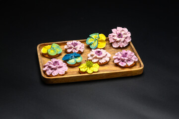 Cookies decorated with sugar flowers in different colors. Cookies on a wooden rectangular plate. Black background with a single light source.