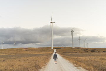 Wind farm with windmills. A person is walking along a path to the windmills. Renewable energy...