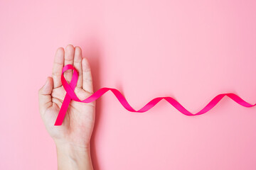 October Breast Cancer Awareness month, adult Woman hand holding Pink Ribbon on pink background for...