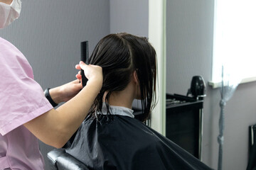 Hairdresser in medical mask creating a hairstyle for young woman in beauty salon. Beauty salon services work during the quarantine period covid 19