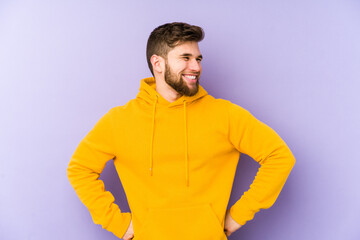 Young man isolated on purple background laughs happily and has fun keeping hands on stomach.