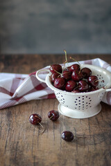 Cerezas en un colador blanco, sobre mesa de madera, con fondo liso. Vista aérea.