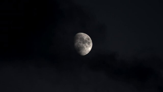 Sharp image of the moon in its first quarter, detail of the texture as the black clouds cross in the middle of the night.