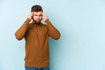 Young caucasian man isolated on blue background touching temples and having headache.