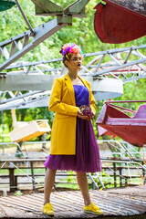 Fashion model in a yellow coat posing against the backdrop of amusement park