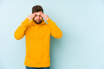 Young caucasian man isolated on blue background having a head ache, touching front of the face.