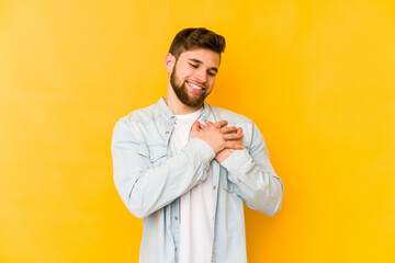 Young caucasian man isolated on yellow background has friendly expression, pressing palm to chest. Love concept.