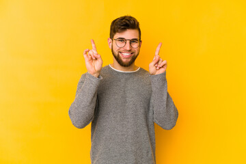 Young caucasian man isolated on yellow background indicates with both fore fingers up showing a...