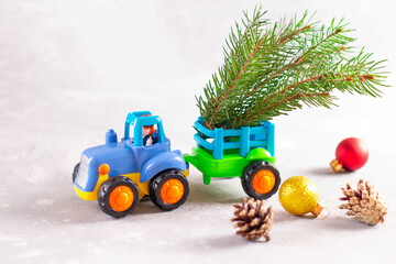 Toy tractor carrying a Christmas tree with fir branch, fir cone