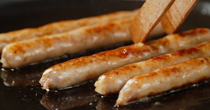 Fried sausage is turned over on pan with a wooden spatula. 