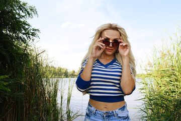 Young woman in a striped sweater wearing sunglasses near the lake