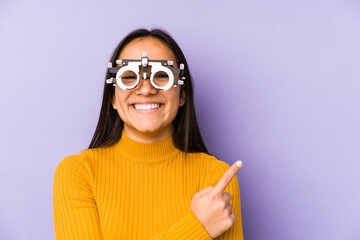 Youn indian woman with optometry glasses smiling cheerfully pointing with forefinger away.