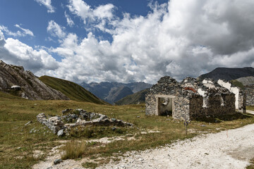 Fototapeta na wymiar In the foreground a mountain pass in the alps ruins of a mitilitaries customs house between France and Italy. In the background the mountains, the clouds and the blue sky,