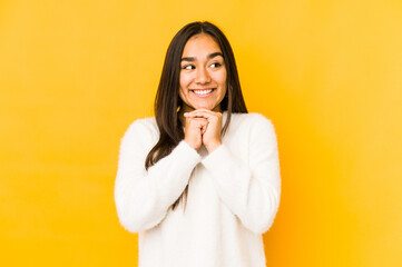 Young woman isolated on a yellow background keeps hands under chin, is looking happily aside.