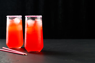 Refreshing summer mocktails with ice cubes. Two tall glasses of iced red juice with straws on dark background. Copy space