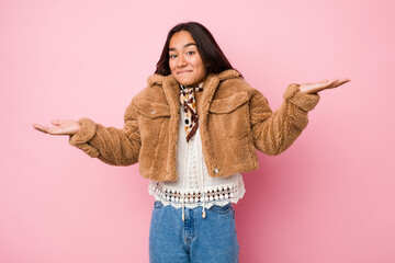 Young mixed race indian woman wearing a short sheepskin coatdoubting and shrugging shoulders in...