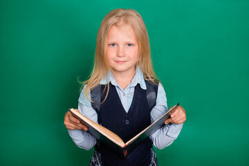 Girl in school uniform with book in hands isolated on green background.